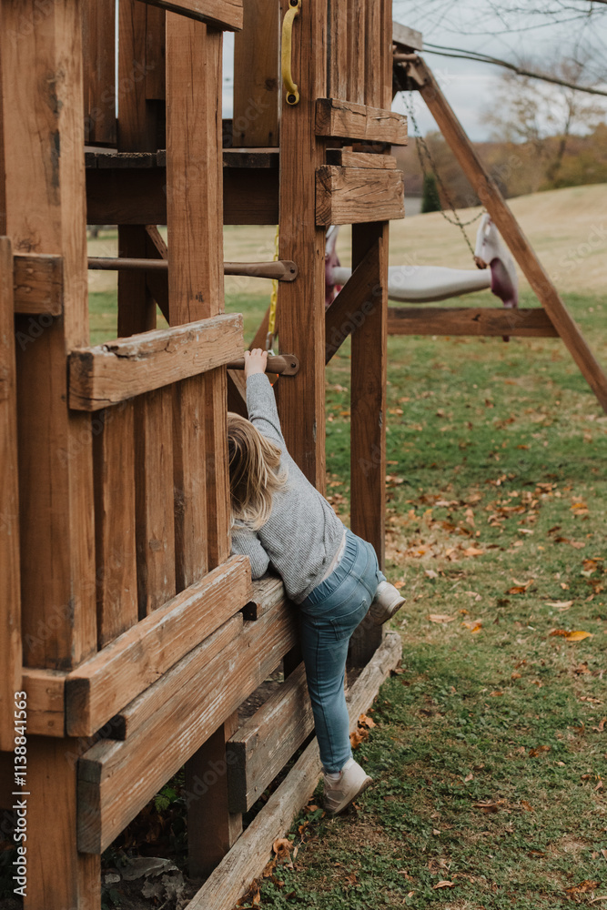 Young child climbing on a wooden outdoor play structure in a grassy park, showcasing adventurous playtime and childhood exploration in a natural setting with wooden playground equipment Young child climbing on a wooden outdoor play structure in a grassy park, showcasing adventurous playtime and childhood exploration in a natural setting with wooden playground equipment
