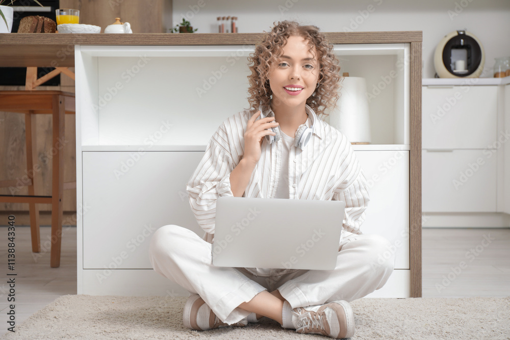 Young woman with headphones and laptop sitting on floor in kitchen Young woman with headphones and laptop sitting on floor in kitchen
