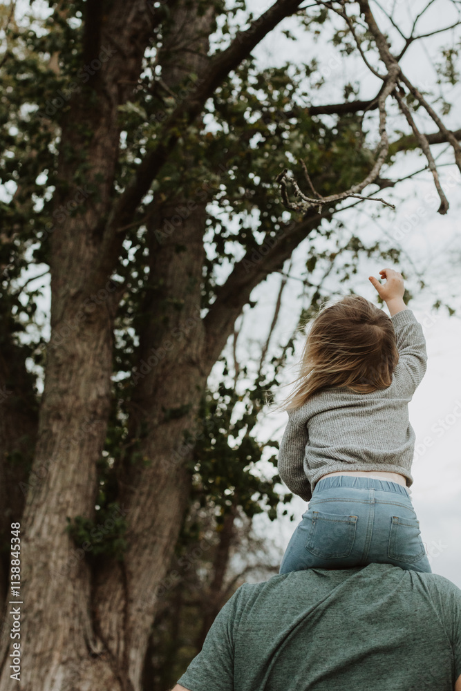 Young child on parent’s shoulders reaching for tree branches during a joyful outdoor moment in a natural park setting, symbolizing curiosity, exploration, and carefree childhood fun among nature Young child on parent’s shoulders reaching for tree branches during a joyful outdoor moment in a natural park setting, symbolizing curiosity, exploration, and carefree childhood fun among nature