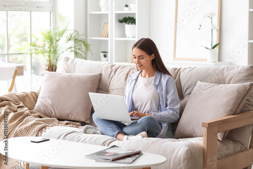 Beautiful young happy woman with laptop sitting on sofa at home