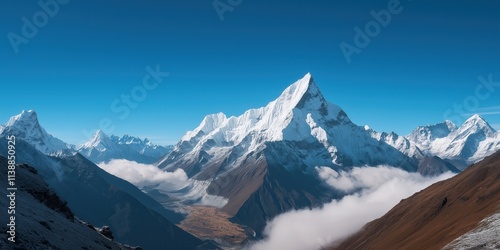 A wide-angle shot of isolated, snow-draped peaks rising dramatically against a crisp blue sky, with a faint layer of mist hovering in the valleys below photo