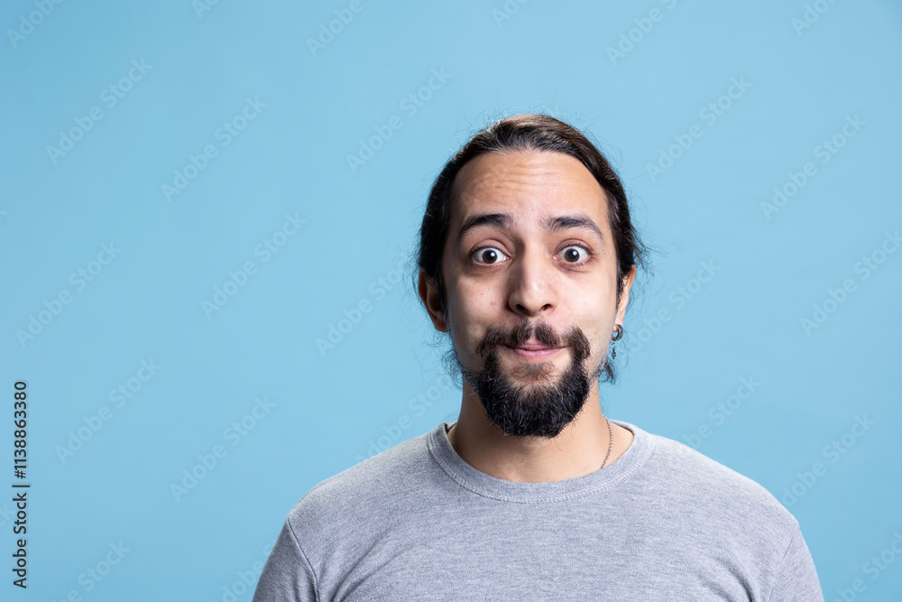 Obraz premium Male model with long curly hair posing with confidence in studio, standing with his casual wear against blue background. Young peaceful confident man with self assured attitude.