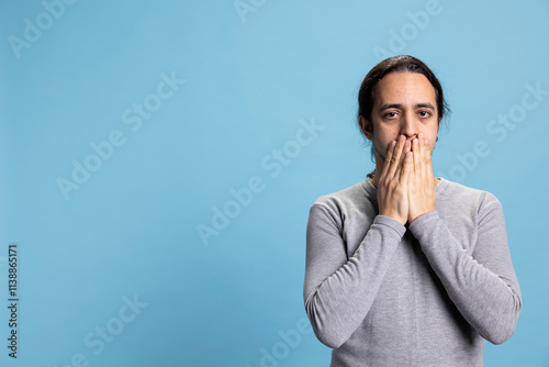 Photography Middle eastern guy doing the three wise monkeys symbol and covering his mouth, speak no evil as a motivational metaphor against blue background