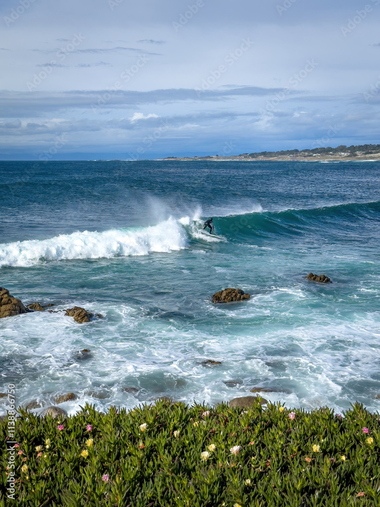 Surfer riding a wave in the Pacific Ocean near Spanish Bay Vista Point, Del Monte Forest, California, USA against blue sky with clouds