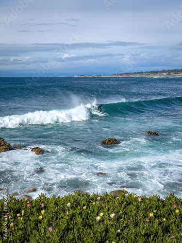Obraz na płótnie Surfer riding a wave in the Pacific Ocean near Spanish Bay Vista Point, Del Monte Forest, California, USA against blue sky with clouds w salonie