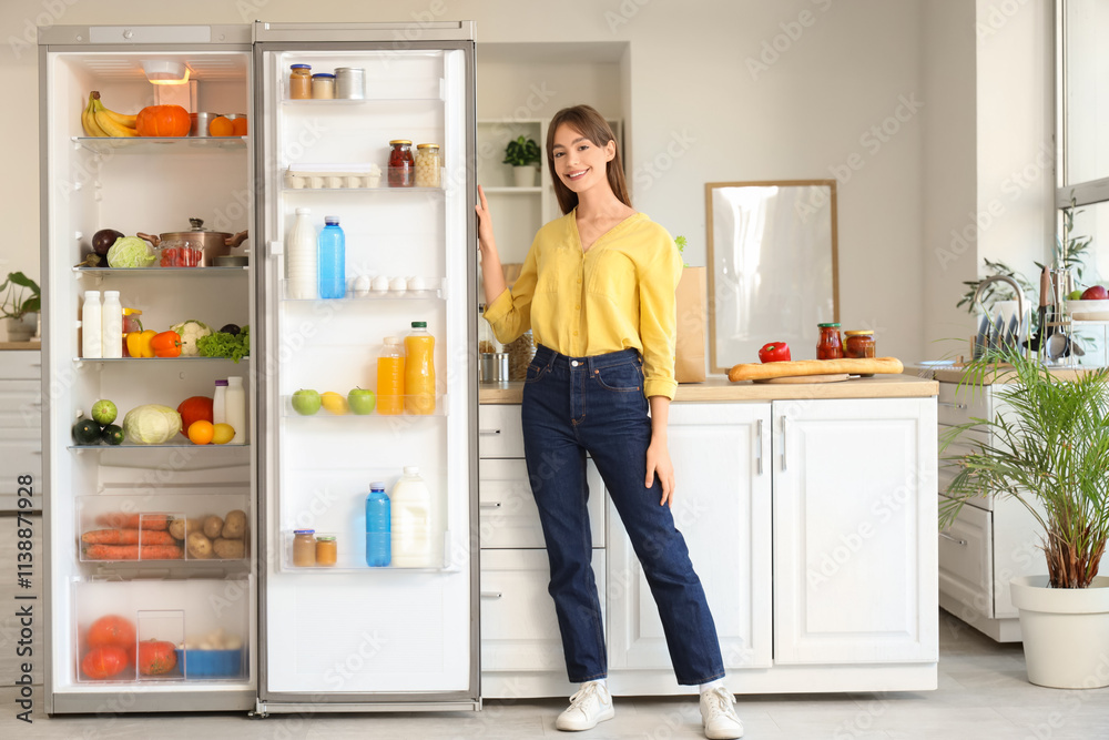 Young woman near open fridge with many products in kitchen Young woman near open fridge with many products in kitchen