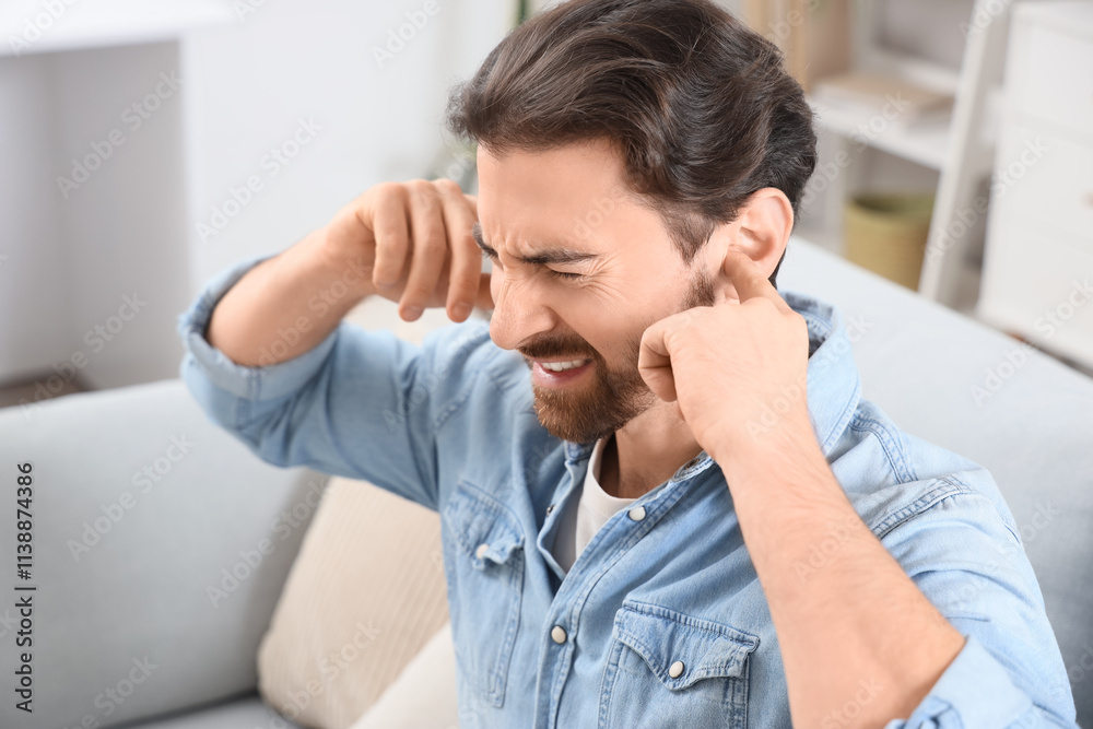 Young man with hearing problem covering his ears on sofa at home, closeup Young man with hearing problem covering his ears on sofa at home, closeup