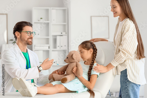 Male pediatrician vaccinating girl with toy bear and mother in clinic photo