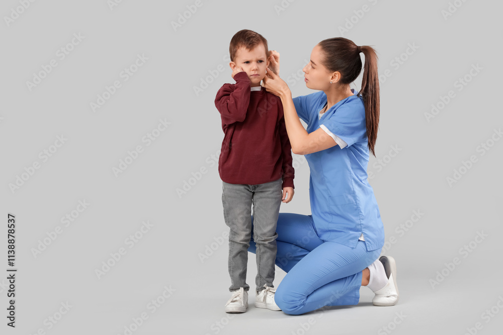 Female doctor examining little boy's ear with hearing problem on light background Female doctor examining little boy's ear with hearing problem on light background