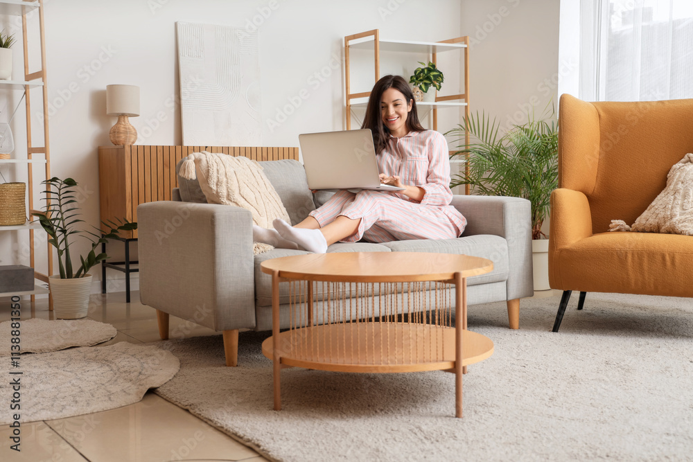Young woman in striped pajamas working with laptop on sofa at home Young woman in striped pajamas working with laptop on sofa at home