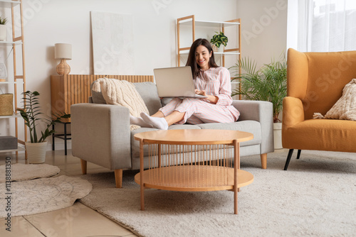 Young woman in striped pajamas working with laptop on sofa at home