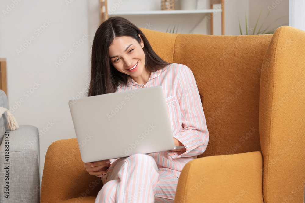 Young woman in striped pajamas working with laptop on armchair at home Young woman in striped pajamas working with laptop on armchair at home