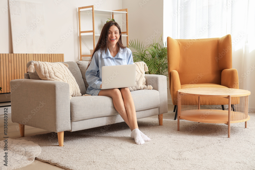 Young woman in blue pajamas working with laptop on sofa at home Young woman in blue pajamas working with laptop on sofa at home