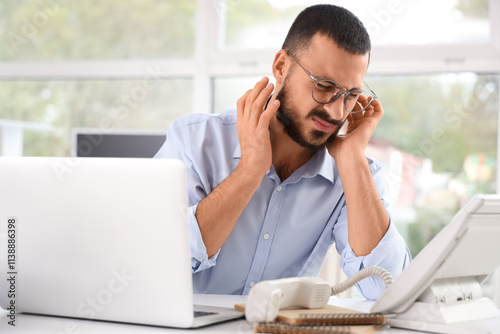 Young businessman suffering from ear pain at table in office