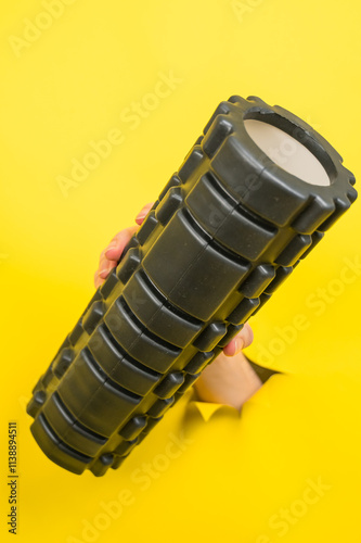 Female hand sticking out with MFR roller from yellow paper background. Vertical photo.  photo