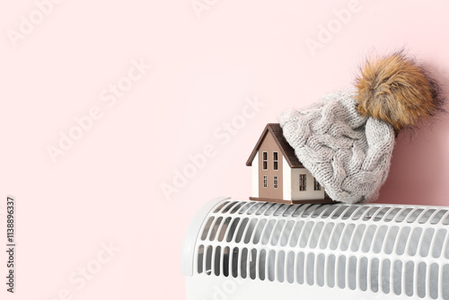 House model with warm hat on convector heater against pink background. Heating saving concept photo