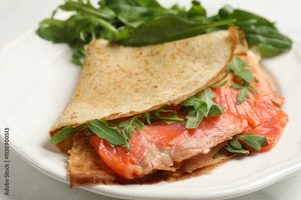 Delicious crepes with salmon and arugula on white table, closeup Delicious crepes with salmon and arugula on white table, closeup