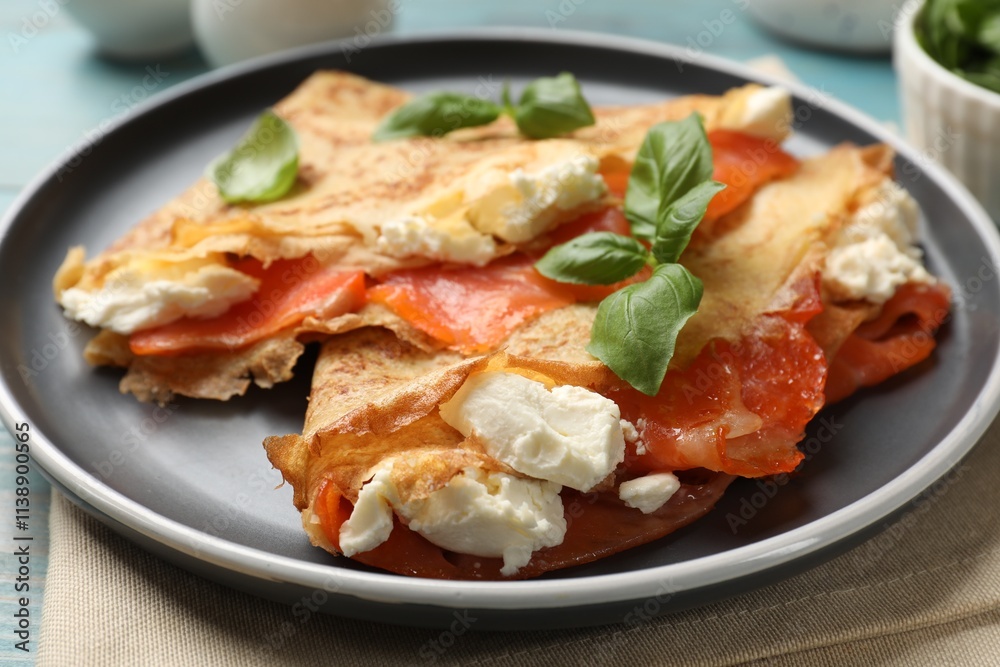 Delicious crepes with salmon, cream cheese and basil on table, closeup Delicious crepes with salmon, cream cheese and basil on table, closeup