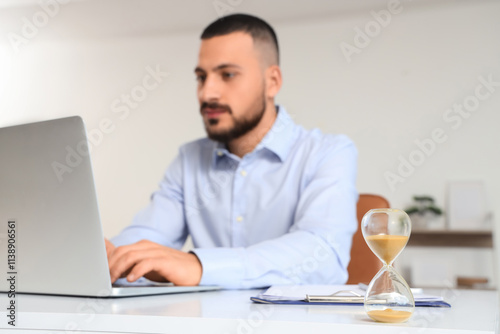 Hourglass on desk against businessman working with laptop in office, closeup