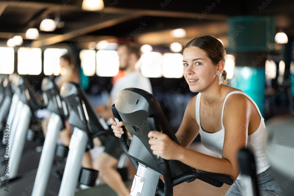 Fototapeta premium Young athletic woman working out on exercise bike in gym