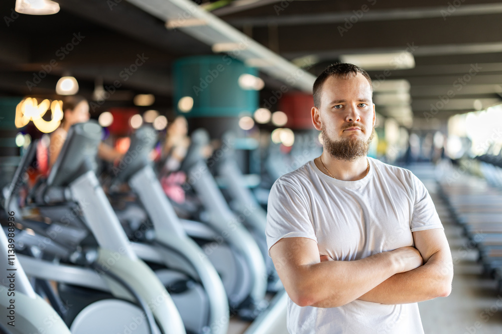 Fototapeta premium Young guy trainer in sportswear poses in middle of fitness center gym. Active lifestyle, daily workouts in crossfit gym