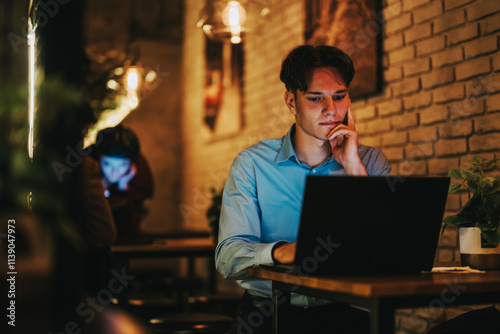 A business person intensely focused on a laptop, working late hours in a warm and cozy coffee shop, surrounded by ambient lighting and a casual atmosphere. photo