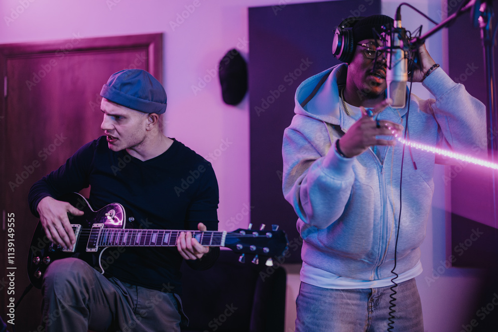 Obraz premium Musicians in a recording studio, one playing guitar and the other singing, capture the creative energy of music collaboration. The modern setup enhances the dynamic atmosphere of their performance.