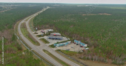 An expansive view of highway intersection featuring gas stations and shops surrounded by dense forest