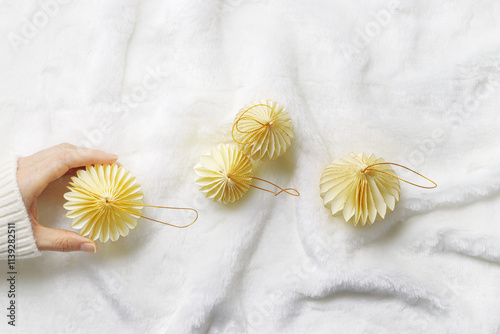 New Year Festive winter holidays concept, Minimal style top view aesthetic layout with hand holding cream beige paper ornaments, Christmas balls on white fluffy fur background, creative flat lay