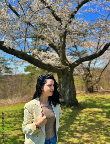 Beautiful black haired young woman in white jacket enjoying cherry blossom season at the park.