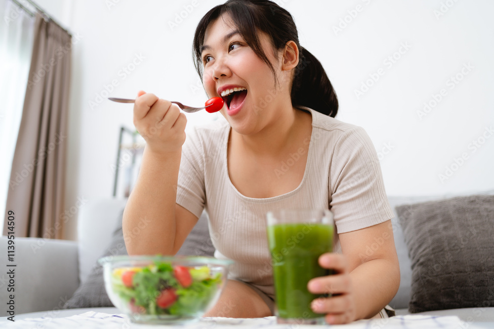 Beautiful Asian woman eating salad, holding a glass bowl and using a fork to pick up a tomato to eat Beautiful Asian woman eating salad, holding a glass bowl and using a fork to pick up a tomato to eat