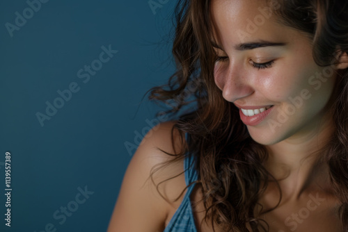 Portrait photo of a latina hispanic female model looking down at something with a smiling face isolated on a blue background
