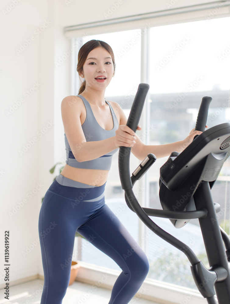 Fototapeta premium Asian young beautiful cheerful happy woman active girl in sportswear stationary exercise bike movement speed energy training in fitness gym or living room at home, healthy wellness action lifestyle