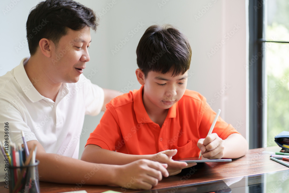 Obraz premium Father helping his son doing homework and drawing on tablet with happiness family moment at home