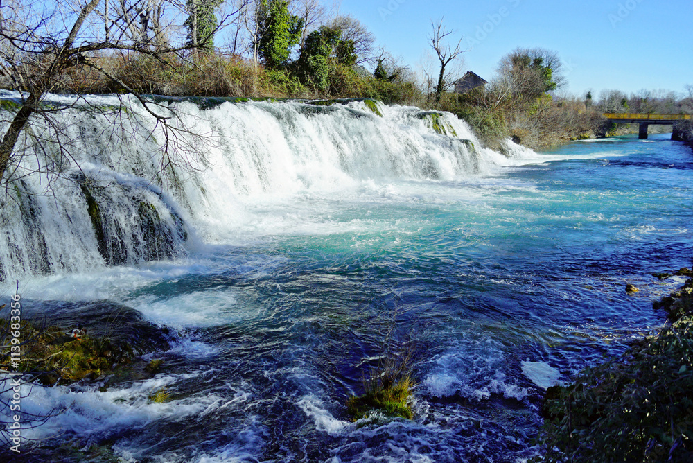 The bright blue waters of the river and the Kocusa waterfall falling into them from a height of several meters, photographed during a trip to the most picturesque places of Bosnia and Herzegovina. The bright blue waters of the river and the Kocusa waterfall falling into them from a height of several meters, photographed during a trip to the most picturesque places of Bosnia and Herzegovina.