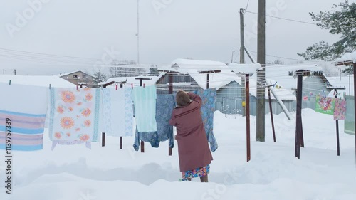 Traditional daily life far from civilization, Grandmother gray downy shawl, felt boots goes hang out laundry washing cold. Clean sheets, freshness winter snow outback, wooden village Russia, Siberia