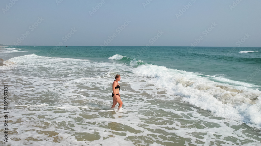 A Caucasian woman in a black bikini enjoys a sunny day at the beach, capturing the essence of summer relaxation A Caucasian woman in a black bikini enjoys a sunny day at the beach, capturing the essence of summer relaxation