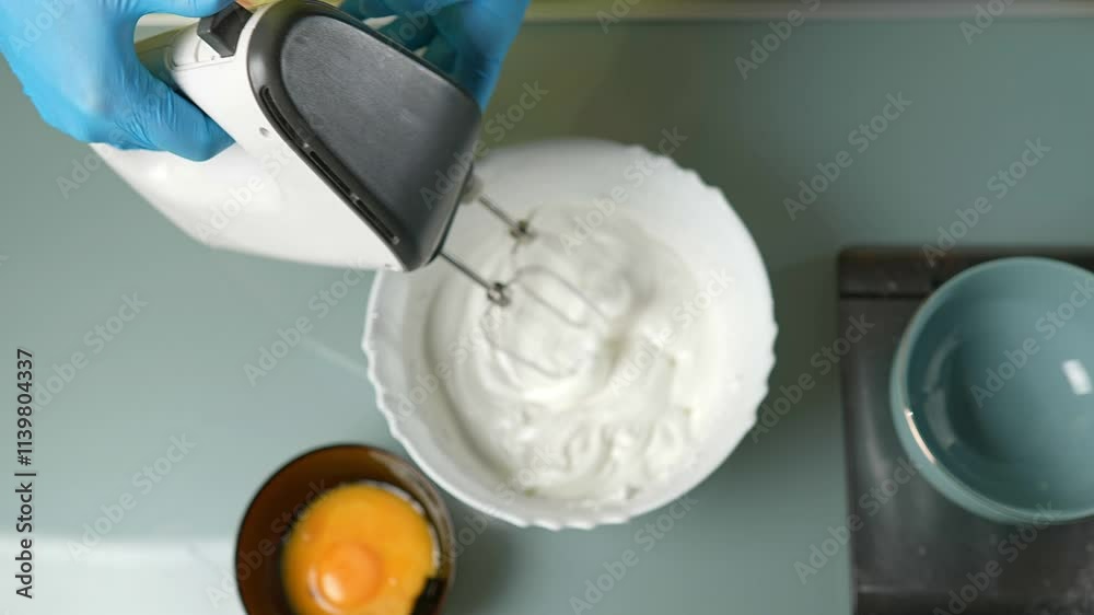 A closeup view of an electric mixer thoroughly blending a creamy batter inside a shiny stainless steel bowl
