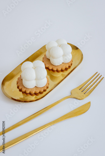 Two White Dessert Cubes on a Gold Stand with Golden Cutlery on a White Background