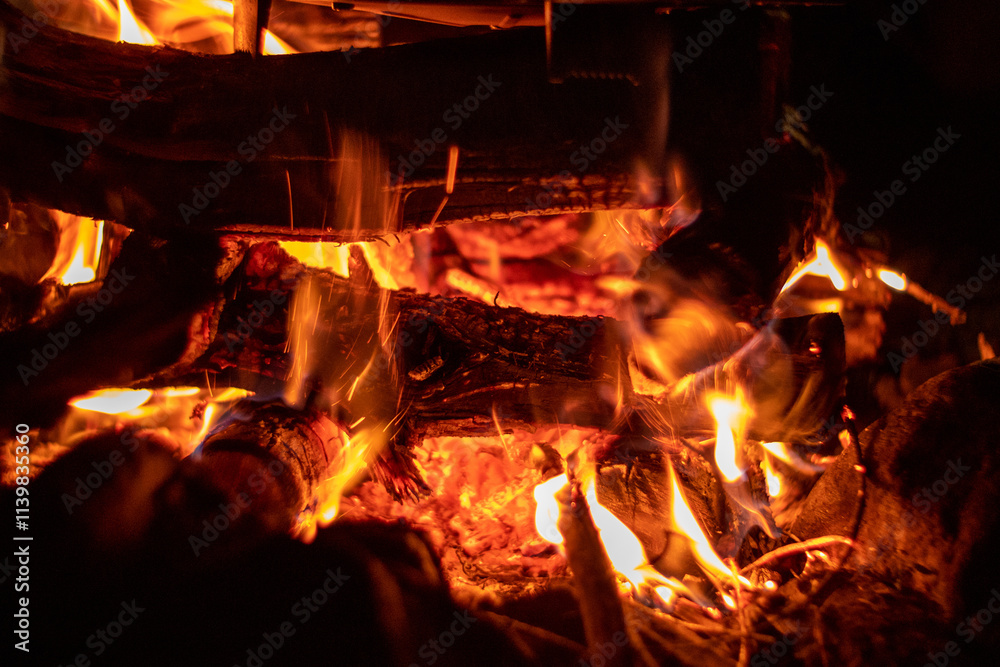 A mesmerizing view showcases glowing embers and flickering flames in a warm and cozy campfire setting, close-up background