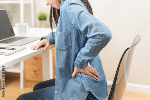 Close-up woman massaging her lower back has back pain because of sitting posture during work in office. photo