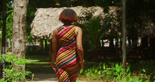 A lively young girl with curly hair, donning a long dress, savors the tranquil atmosphere of a tropical park on the picturesque island of Trinidad. photo