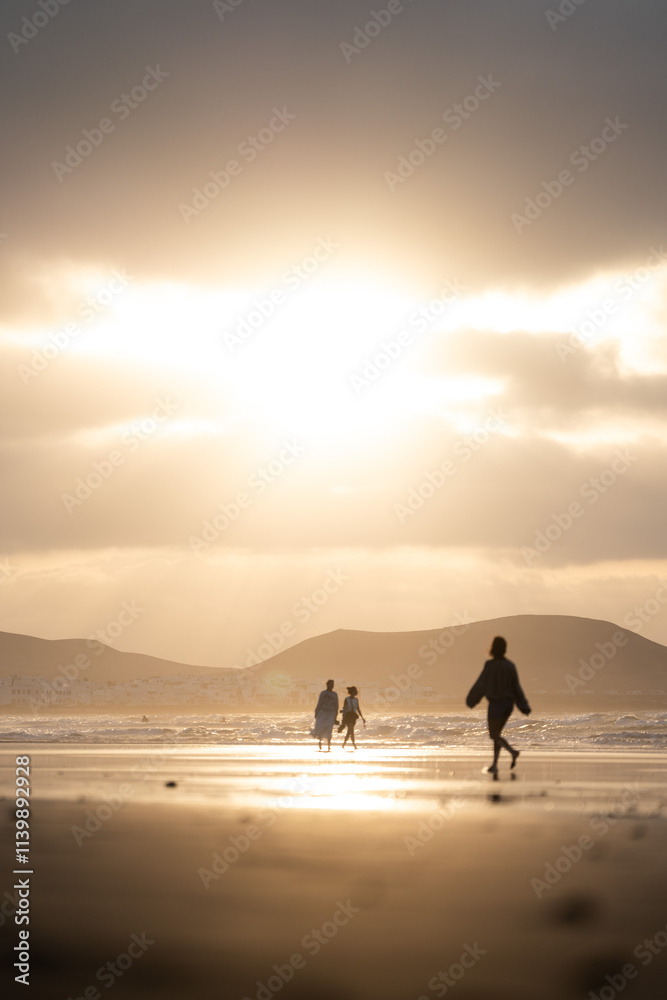 People walking along the beach during sunset with mountains in the background People walking along the beach during sunset with mountains in the background