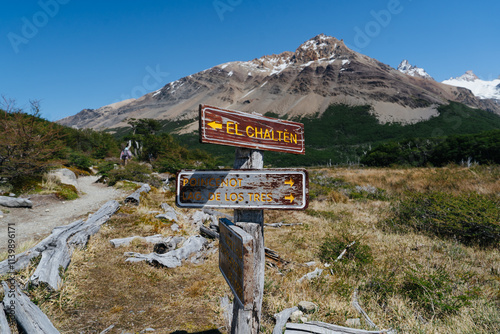 Wooden trail signs point to El Chaltén and Laguna de los Tres, set against a stunning Patagonian backdrop of rugged peaks and golden grasslands