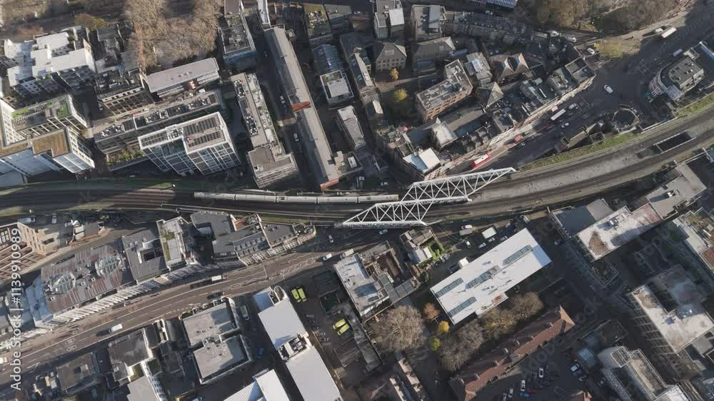 Top-down aerial view of an overground train making its way through London’s bustling streets, capturing urban movement Top-down aerial view of an overground train making its way through London’s bustling streets, capturing urban movement