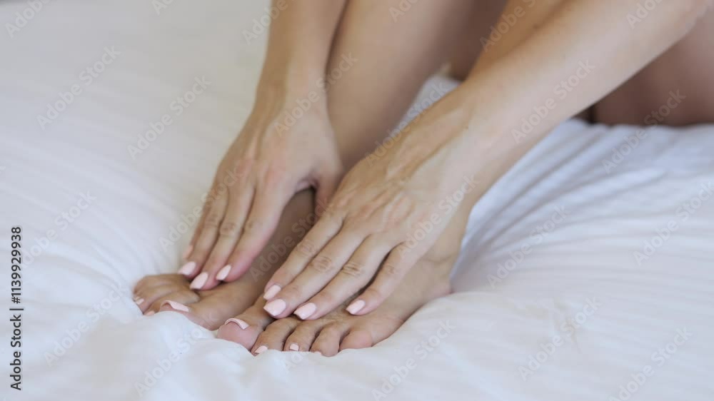 Woman sitting on bed in bedroom rubs feet to relieve tension Close up of feet showing relaxation and self care Perfect for tired legs legs foot care routines Concept of caring for the feet of feet Woman sitting on bed in bedroom rubs feet to relieve tension Close up of feet showing relaxation and self care Perfect for tired legs legs foot care routines Concept of caring for the feet of feet