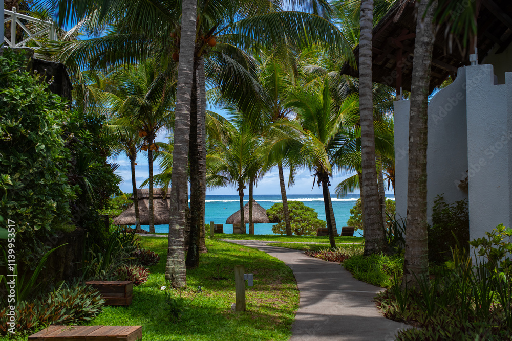 Obraz premium Vacation concept - Path near the cozy cottage. Turquoise Indian ocean and beach in a background. Vacation in a luxury island. Selective focus, blurred background. Belle Mare, Mauritius.