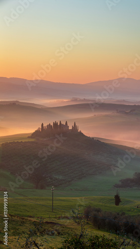 Rolling hills of Tuscany at sunrise, bathed in soft mist in Spring. A serene farmhouse surrounded by cypress trees and lush greenery creates a dreamy, picturesque Italian countryside landscape