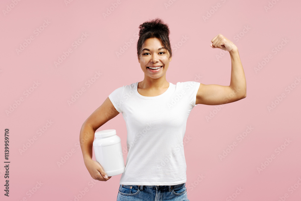 Young woman showing her biceps and holding nutritional supplement on pink background Young woman showing her biceps and holding nutritional supplement on pink background