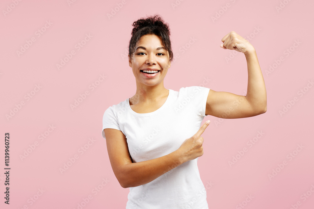 Young woman showing biceps and pointing at it on pink background Young woman showing biceps and pointing at it on pink background